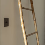 Kipphebelschalter – Bronze – an eine cremefarbene Wand montiert, Leiter aus Bambus rechts. 